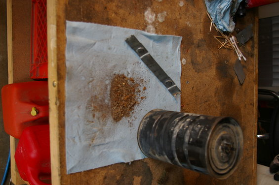 Oil filter and debris on paper towel on workbench, next to red gas cans