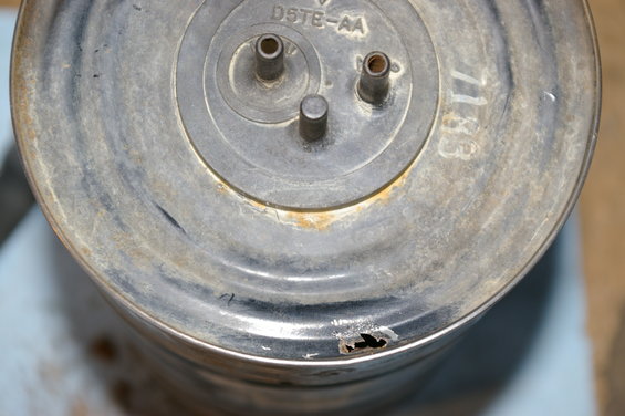 Metal canister with D5TE-AA and 7183 markings, showing rust and a hole