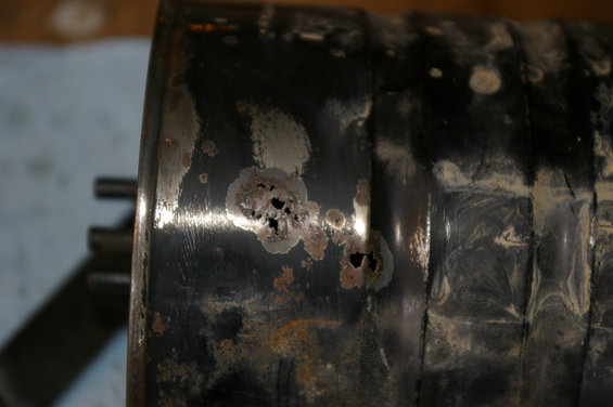 Rusted black metal cylinder with holes, showing wear and tear