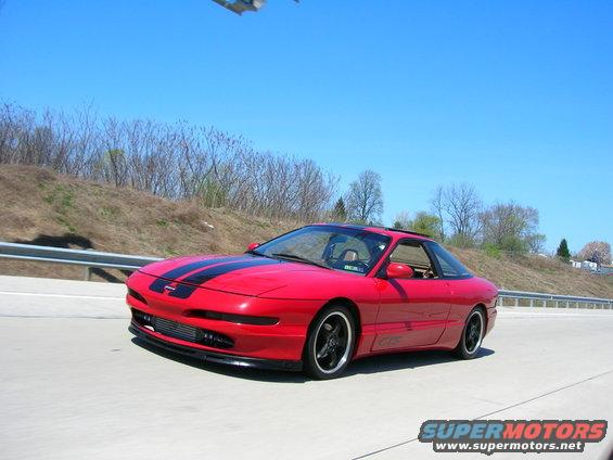 Red 1994 Ford Probe with black racing stripes on the hood, driving on a highway