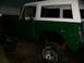 1974 Ford Bronco - A green and white 1974 Ford Bronco is viewed from the rear quarter angle, highlighting its off-road capabilities.