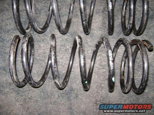 Two pairs of black coil springs on a gray surface. Some springs have white markings