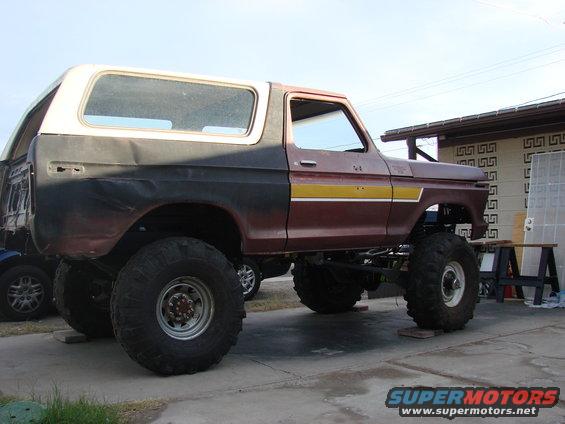 Lifted 1978 Ford Bronco with maroon, yellow, and black paint, sitting on blocks