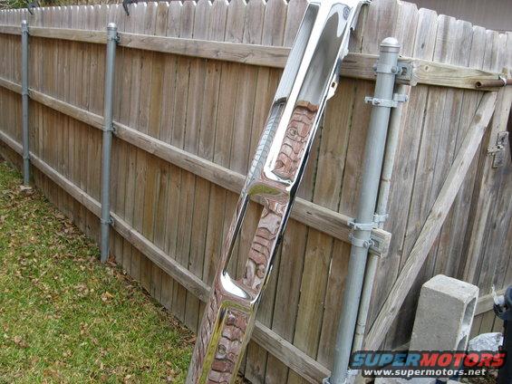 Chrome bumper leaning against a wooden fence, reflecting the fence and sky