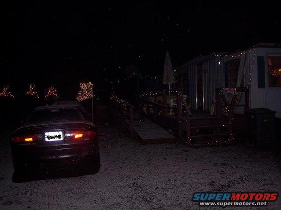 Dark sedan's rear end visible at night with Christmas lights on a trailer home