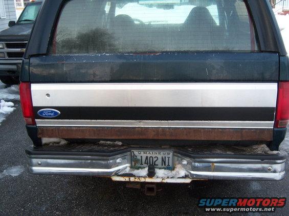 Rear of a dark green Ford Bronco with a silver stripe and a Maine license plate. Another vehicle is parked behind it