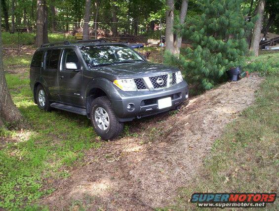 Dark gray Nissan Pathfinder parked on a dirt path next to trees and grass
