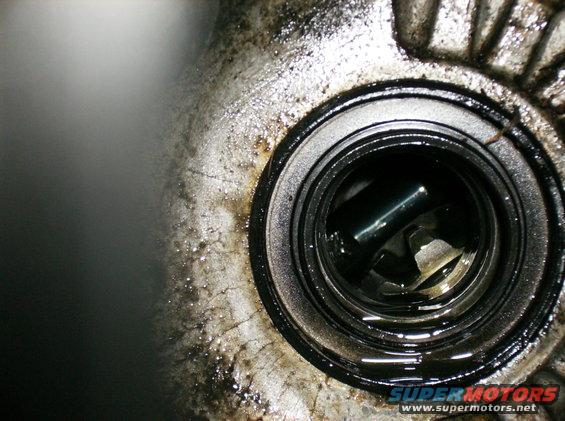 Close-up of a greasy engine part with a circular opening showing internal components