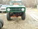 1974 Ford Bronco - Front view of a green 1974 Ford Bronco, lifted with large tires. A white Jeep is visible behind it.