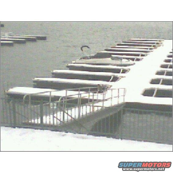 Boats covered in snow docked at a marina with a ramp and railing