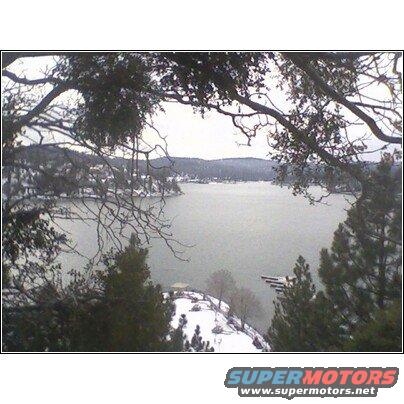 Snowy landscape with a lake and trees, framed by branches
