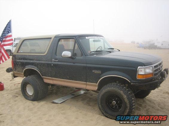 1995 Ford Bronco with tan top on sand, American flag on left