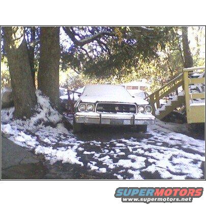 1972 Ford Ranchero covered in snow, front view, parked on a driveway with trees and a yellow staircase