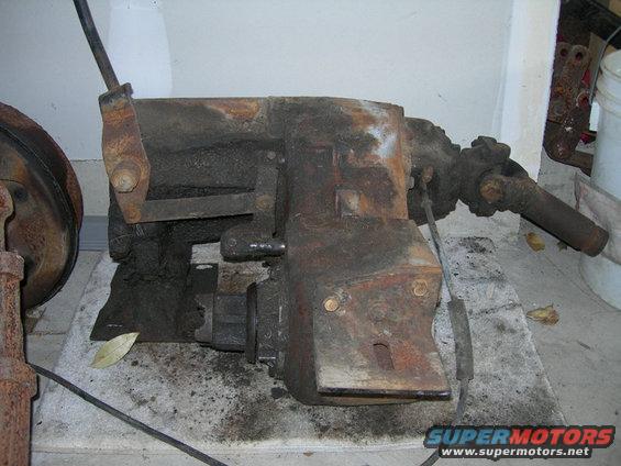 rusty transfer case with linkage and driveshaft attached, sitting on concrete