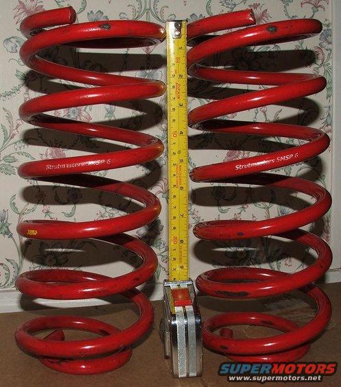 Two red coil springs next to a tape measure. Text on springs reads "Strutmasters SMSP 6"