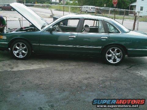 Green 1995 Ford Crown Victoria sedan with hood open, chrome wheels, side view
