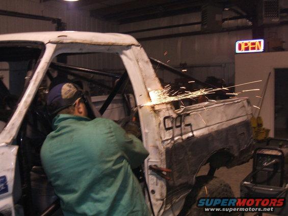Person welding on the side of a white Ford Bronco body, sparks flying. Numbers '995' are visible on the rear quarter panel