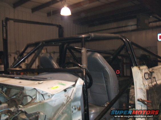 Vehicle interior with a black roll cage installed over the seats. The dashboard area is partially disassembled