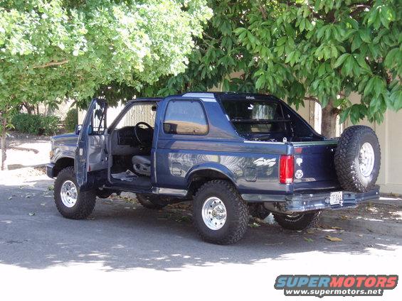 Blue SUV with doors open, spare tire on rear. Appears to be a Ford Bronco