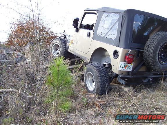 Tan Jeep TJ with soft top on rough terrain, rear view showing spare tire and license plate C14 GGF