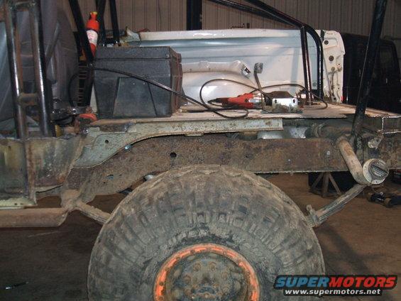 Side view of heavily rusted vehicle frame and large tire with orange rim
