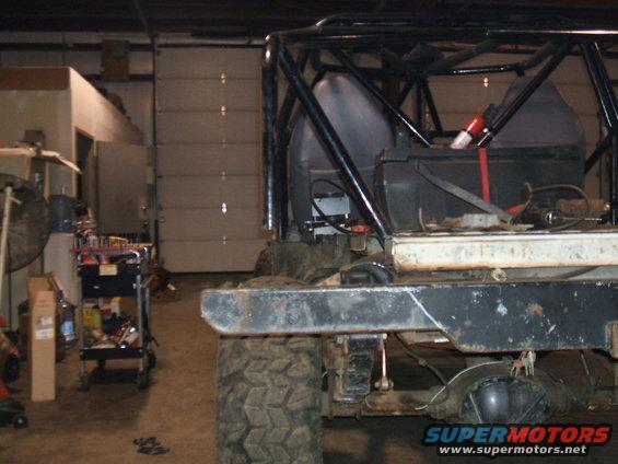 Off-road vehicle interior with roll cage, battery, and seats visible. Rear axle and tire also in view