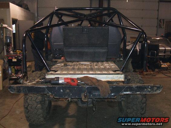 Rear view of a modified SUV with a large external roll cage, tool, and glove on the bumper