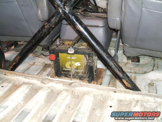 Battery and roll cage inside a vehicle's interior, showing worn seats and floor