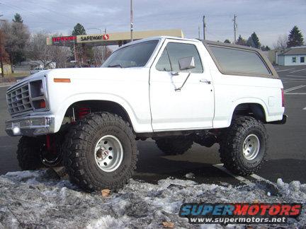 White lifted Ford Bronco parked in a snowy lot, Safeway store in background