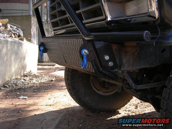 Front bumper with diamond plate texture and blue tow hooks on a truck, grille visible above