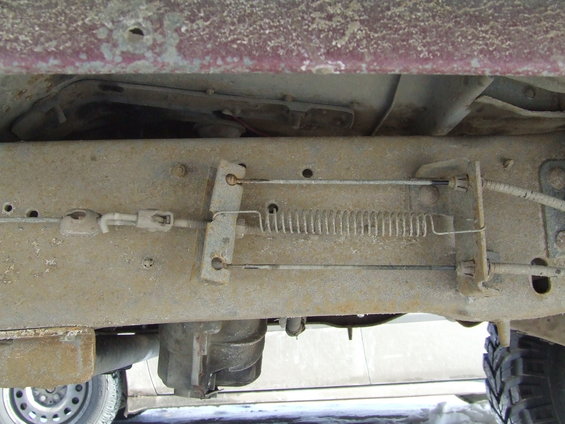 Underside of a vehicle showing brake cables and a spring mechanism attached to the frame