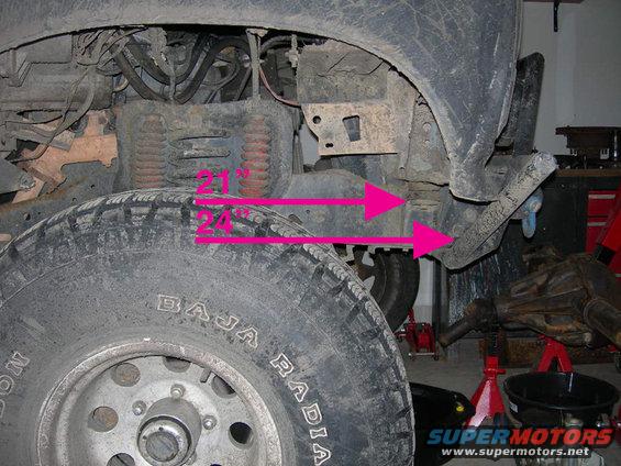 Close-up of vehicle suspension with measurements marked by pink arrows. Tire tread reads 'BAJA RADIAL'