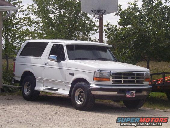 White 1996 Ford Bronco parked on gravel, front 3/4 view, with a sun visor and American flag plate