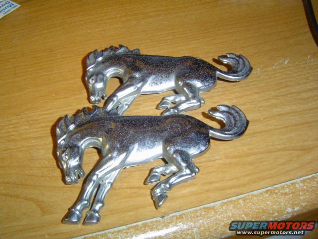 Two chrome horse emblems on a wooden surface