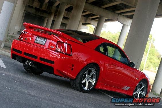 Red 2004 Saleen S-281SC Mustang coupe parked under concrete overpass, rear 3/4 view