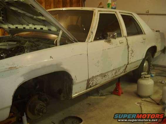 White sedan on jack stands, hood open, showing rust and primer on body panels