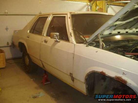 White sedan with hood open, showing engine bay and rust on wheel well