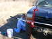 1996 Ford Bronco - A man kneels beside a dark blue 1996 Ford Bronco, operating a red Hi-Lift jack near the front tire.