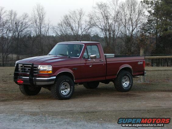 Maroon Ford F-150 pickup truck with a chrome grille guard, lifted suspension, and off-road tires