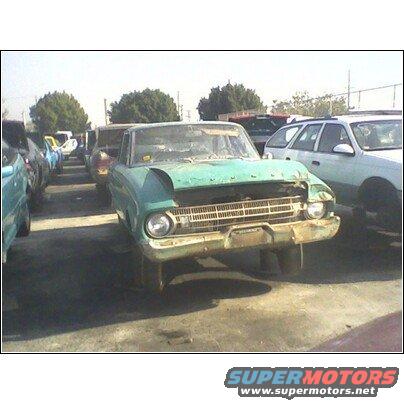 Front view of a beat-up green 1960s car in a junkyard with other cars around