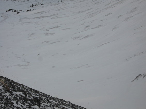Wide shot of a snow-covered mountain slope with some rocky areas in the foreground