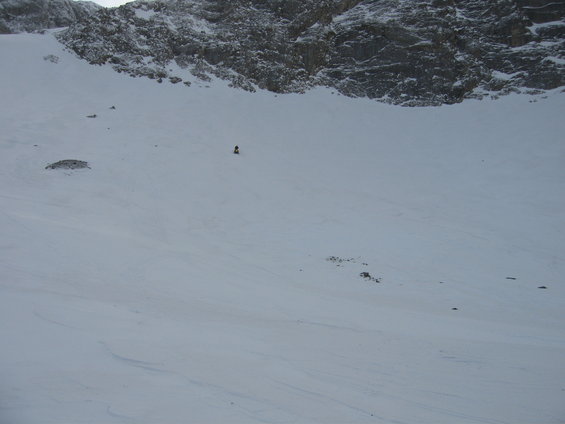 Distant figure on a vast, snow-covered mountain slope under a rocky cliff