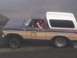 1978 Ford Bronco - A person in a two-tone brown and tan Ford Bronco makes a hand gesture while driving on a dirt road.