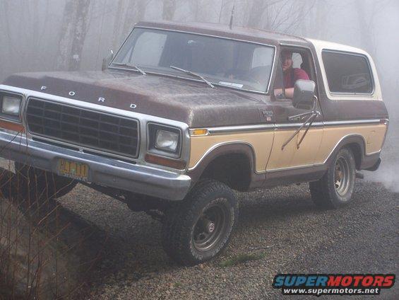 Brown and tan 1978 Ford Bronco with a white top, angled on a gravelly surface with fog in the background