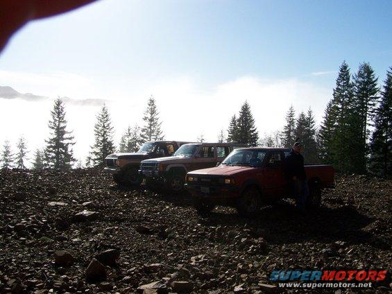 Red pickup truck and two SUVs parked on rocky terrain