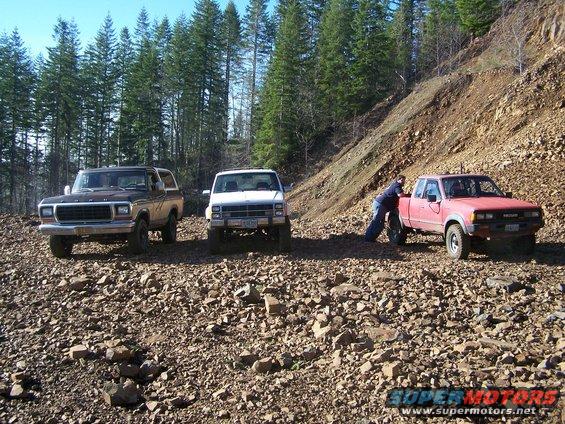 1978 Ford Bronco, white pickup, and red Nissan pickup on a rocky slope with trees