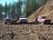 1978 Ford Bronco - Three off-road vehicles parked on a gravelly hillside with a forest in the background.