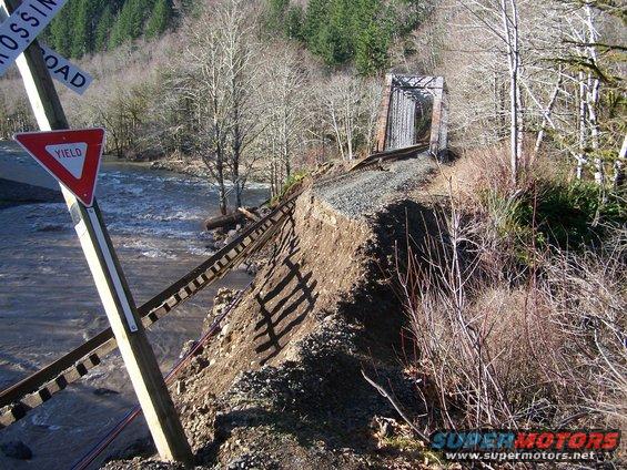 Railroad tracks washed out by a river, with a bridge in the background