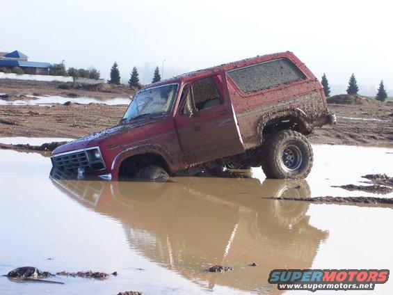 Red Ford Bronco stuck deep in mud, front wheels submerged