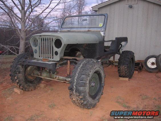 Jeep body on frame with large tires, undergoing restoration. Windshield frame is visible